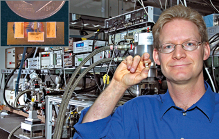 Mike Wanke holds a miniaturised laser device (inset shows it next to a coin) that will eventually replace large pieces of equipment like those in the background